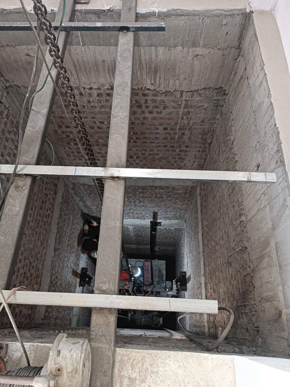 Thi công lắp đặt hố thang máy với khung thép, xích treo và hệ thống máy kéo trong tòa nhà xây thô